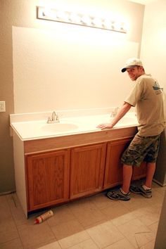 a man standing in front of a bathroom sink with his hands on the counter top