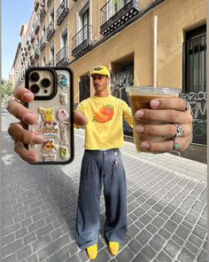 a man in yellow shirt holding up a cell phone with stickers on the back