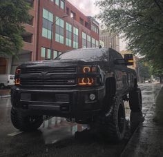 a large black truck parked on the side of a road next to a tall building