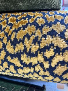 an upholstered blue and gold fabric with small yellow flowers on it, next to a pile of green rugs