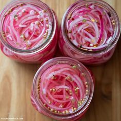 three jars filled with red onions on top of a wooden table