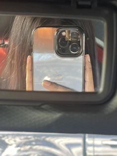 a woman taking a selfie with her cell phone in the rear view mirror while driving