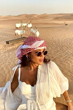 a woman sitting on top of a sandy beach next to animals in the background,