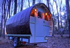 a small white trailer parked in the woods at night with lights on it's windows