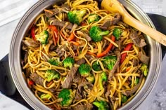 a pot filled with beef and noodles on top of a stove next to a wooden spoon