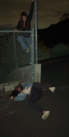 a man laying on the ground next to a fence with a woman standing behind him