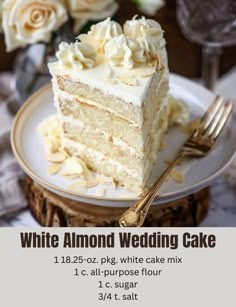 a piece of white wedding cake on a plate with a fork and flowers in the background