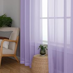 a living room with purple sheer curtains and a chair in front of a window that has a potted plant on it