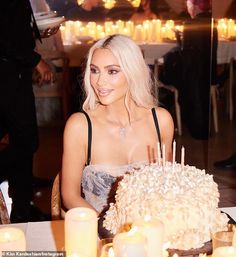 a woman sitting at a table with a cake in front of her and candles around her