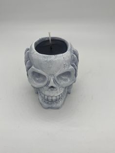 a candle holder with a skull face on the front and side, sitting on a white surface