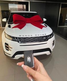 a person holding a cell phone in front of a white car with a red bow on it