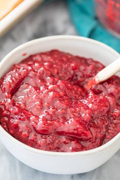 a white bowl filled with cranberry sauce on top of a counter next to a wooden spoon