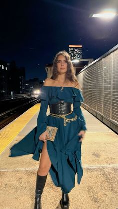 a woman in a blue dress is standing on a train platform at night with her legs spread out