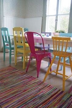 colorful chairs and rugs are arranged around a table in a room with large windows