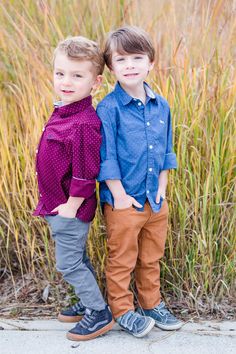 two young boys standing next to each other in front of tall grass