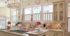 a kitchen with white cabinets and pink flowers on the counter top, chandelier over the stove