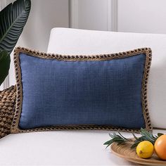 a blue pillow sitting on top of a white couch next to oranges and a plate