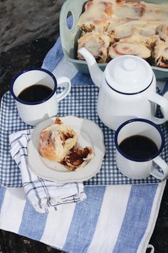 two cups of coffee sit on a blue and white checkered tablecloth with pastries