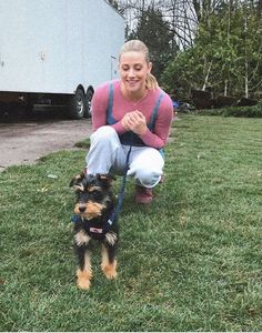 a woman kneeling down next to a small dog