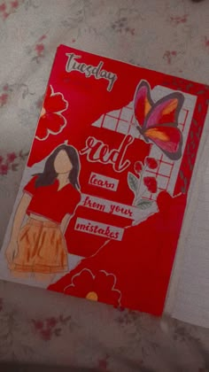 a red notebook with an image of a woman and butterfly on it, sitting on a bed