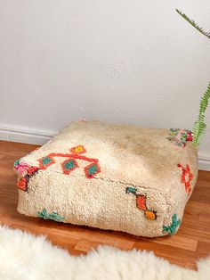 a plant in a pot on top of a footstool that is sitting on the floor