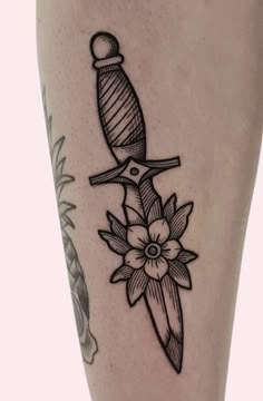 a tattoo on the leg of a person with a knife and flowers in front of it