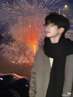 a young man standing in front of a firework display with his scarf around his neck