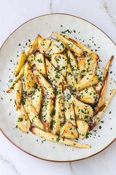 a white plate topped with french fries covered in parmesan cheese and garnished with herbs