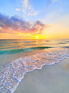 the sun is setting over the ocean with waves coming in to shore and sand on the beach