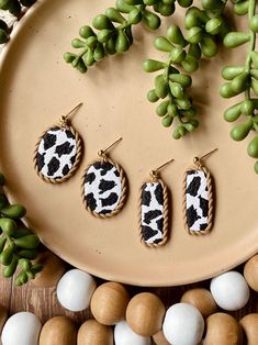 three pairs of animal print earrings sitting on top of a plate next to eggs and plants