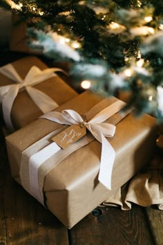 two wrapped presents under a christmas tree with lights on the top and one tied up