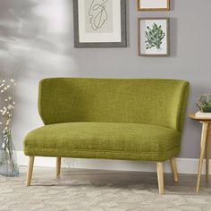 a green couch sitting on top of a wooden table next to a vase filled with flowers