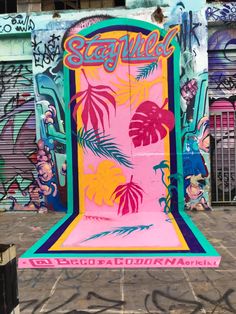 a pink and green sign with palm trees on it in front of graffiti covered buildings