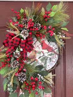 a wreath with red berries, pine cones and evergreens on it hanging from the front door