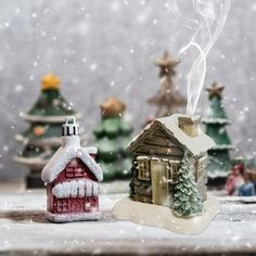 a small toy house next to a tiny christmas tree with snow falling on the ground