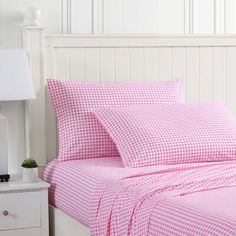 a bed with pink and white checkered sheets in a room next to a night stand