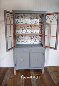 an old china cabinet painted gray with floral wallpaper