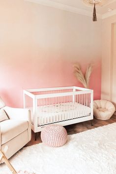 a baby sitting on the floor next to a white crib in a pink room