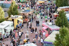 a crowd of people walking around an outdoor food truck park with trucks and food stalls