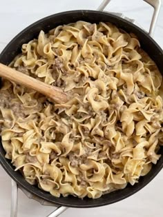 a skillet filled with pasta and meat on top of a white counter next to a wooden spoon