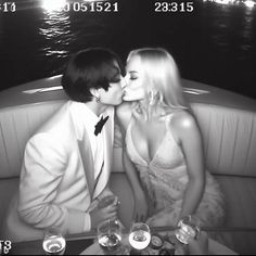 a man and woman kissing on the back of a boat with drinks in front of them