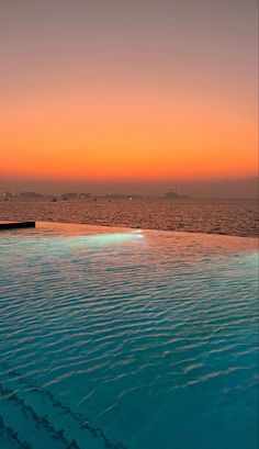 an empty swimming pool with the sun setting over the water and buildings in the distance