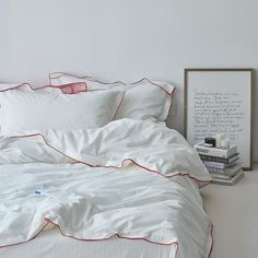 an unmade bed with white sheets and red piping on the pillowcases