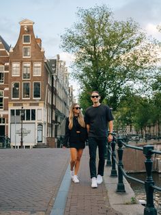 a man and woman walking down a sidewalk next to each other in front of some buildings