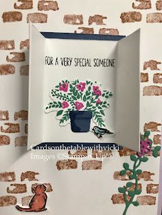 there is a card with flowers and a cat in it on the wall next to a flower pot