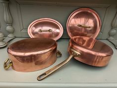 copper pots and pans sitting on top of a counter next to each other with gold handles