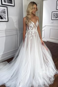 a woman wearing a white wedding dress with sheer tulle and flowers on the skirt