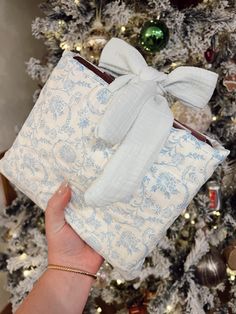 a person holding two wrapped presents in front of a christmas tree with ornaments on it