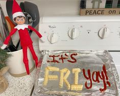 an elf is sitting on top of a stove next to a cake that says it's friday