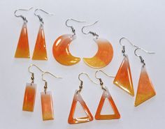 six pairs of earrings are shown on a white surface, including orange and yellow shapes